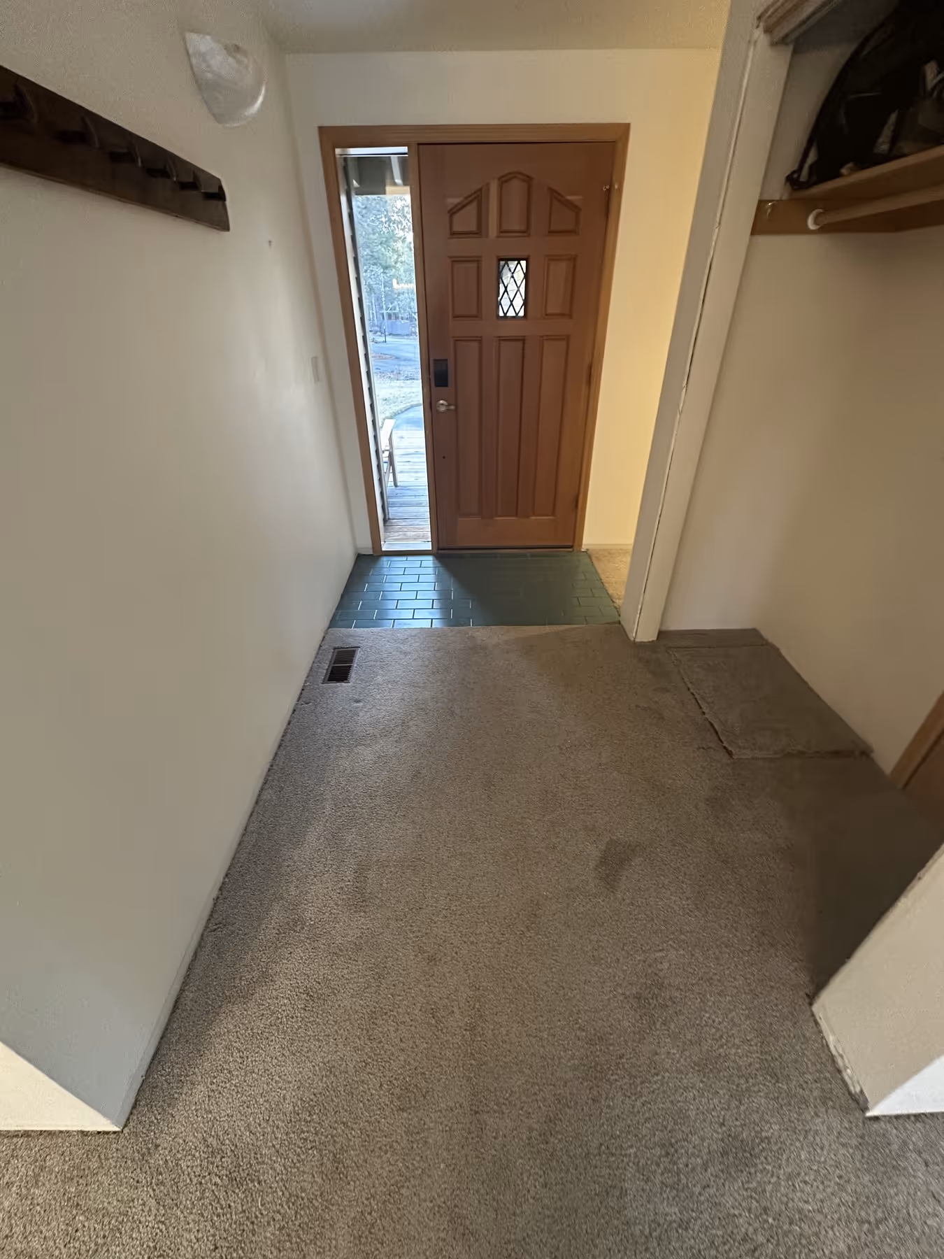 Entryway with a partially open wood front door, green tiled area, and beige carpeted floor with a vent on the left.