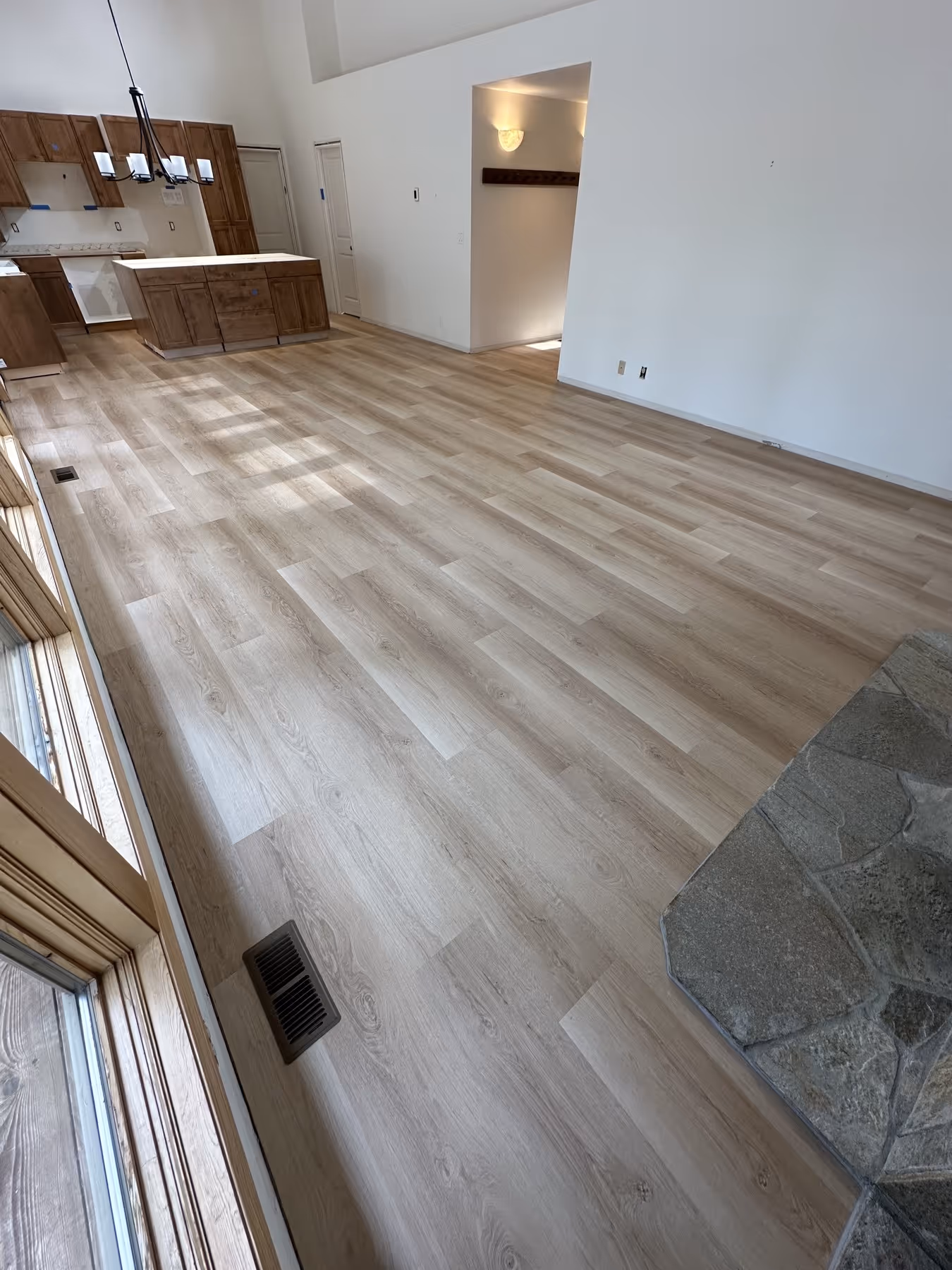 Empty room with light wood laminate flooring, wooden kitchen cabinets, and a stone fireplace hearth on the right.