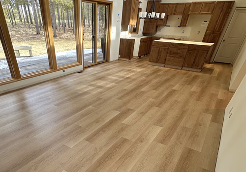 Spacious kitchen with light wood flooring, wooden cabinets, large sliding glass doors, and a view of a wooded outdoor area.