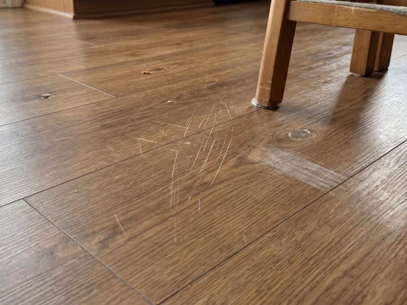Scratched wooden floor near the leg of a wooden chair