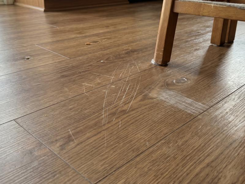 Scratched wooden floor near the leg of a wooden chair