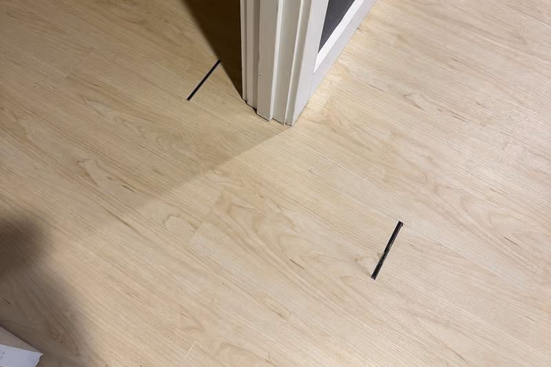 Light wood floor with gaps showing black spaces near a white door frame.