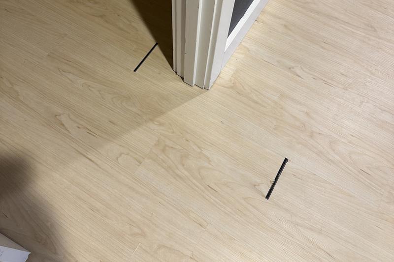Light wood floor with gaps showing black spaces near a white door frame.