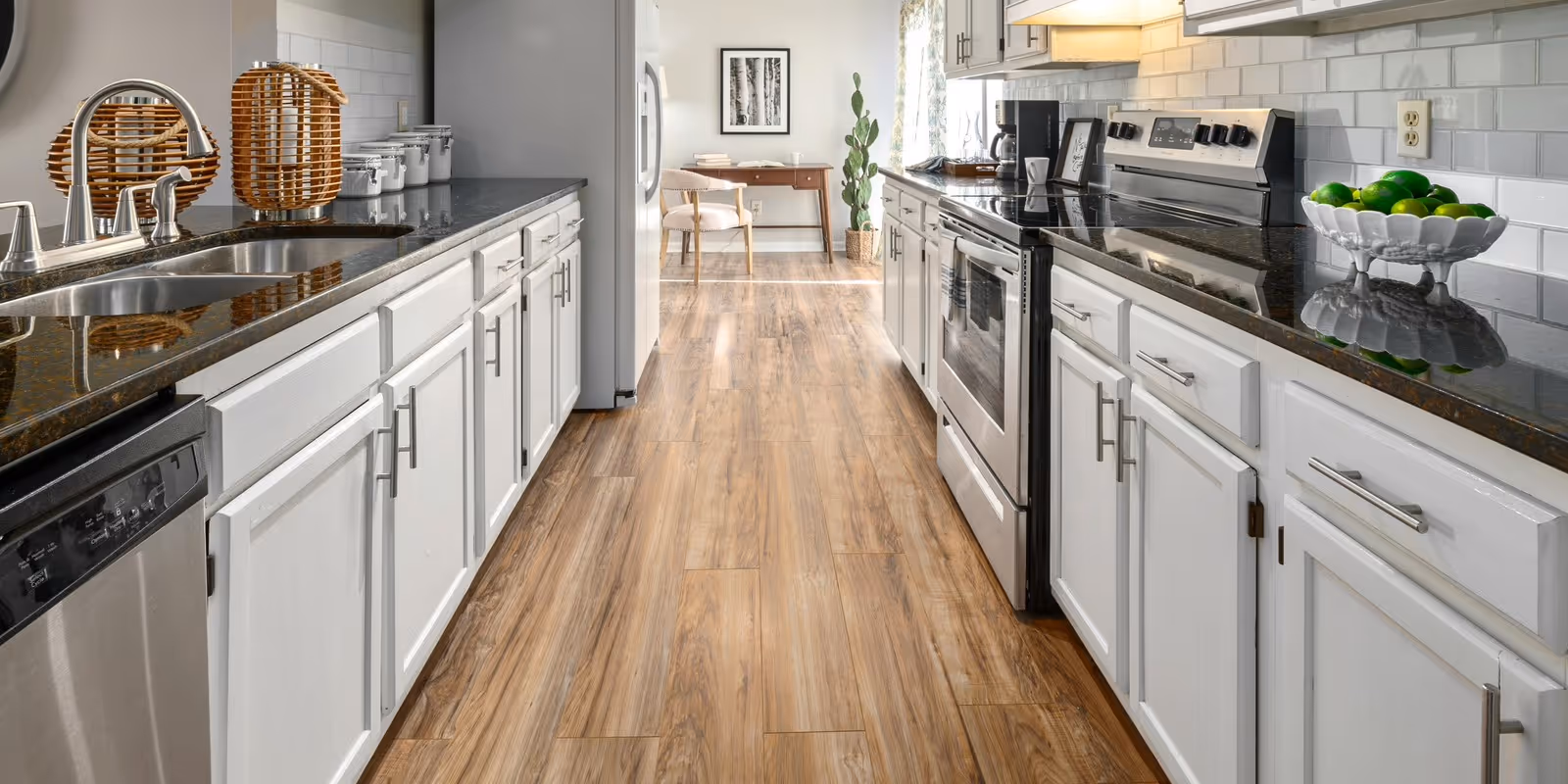 Modern kitchen with white cabinets, wooden floor, stainless appliances, black granite counters, and bright decor.