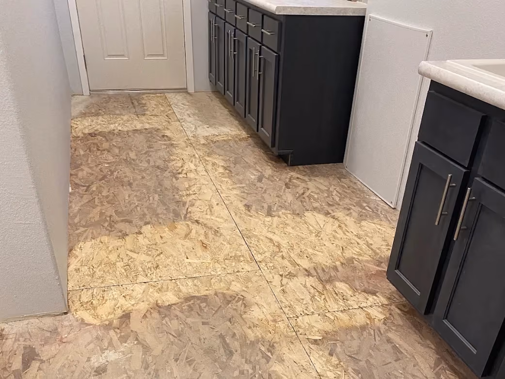 Room with exposed plywood subfloor and dark cabinets along right side under countertops.