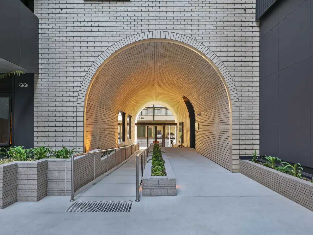 Arched brick tunnel entrance with integrated lighting, flanked by planters and a ramp with handrails.