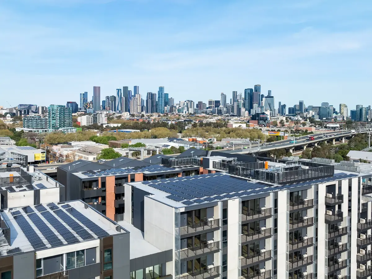 View of modern apartment buildings with solar panels on roofs and a distant city skyline under a clear blue sky.