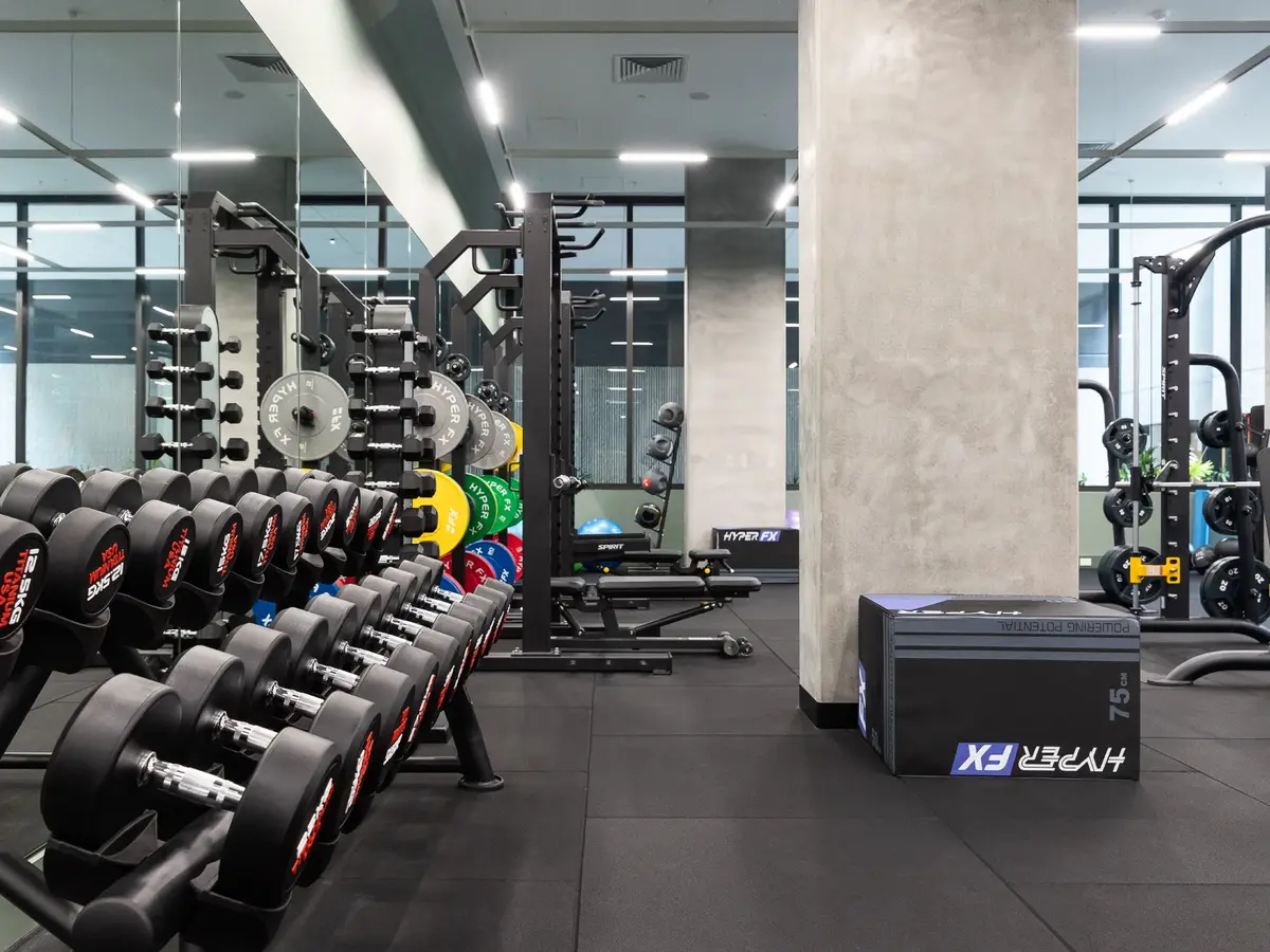 Modern gym interior with rows of dumbbells, weightlifting racks, benches, and a plyometric box labeled Hyper FX.