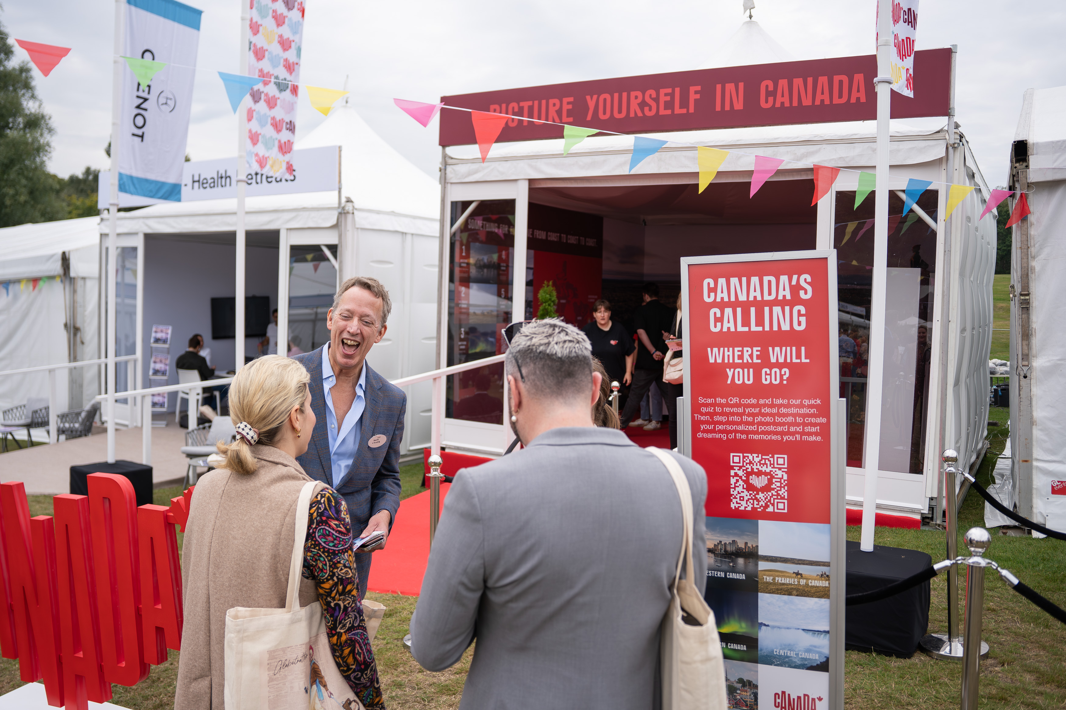 People talking in front of a Canada-themed booth with a sign inviting visitors to scan a QR code to find their ideal Canadian destination.