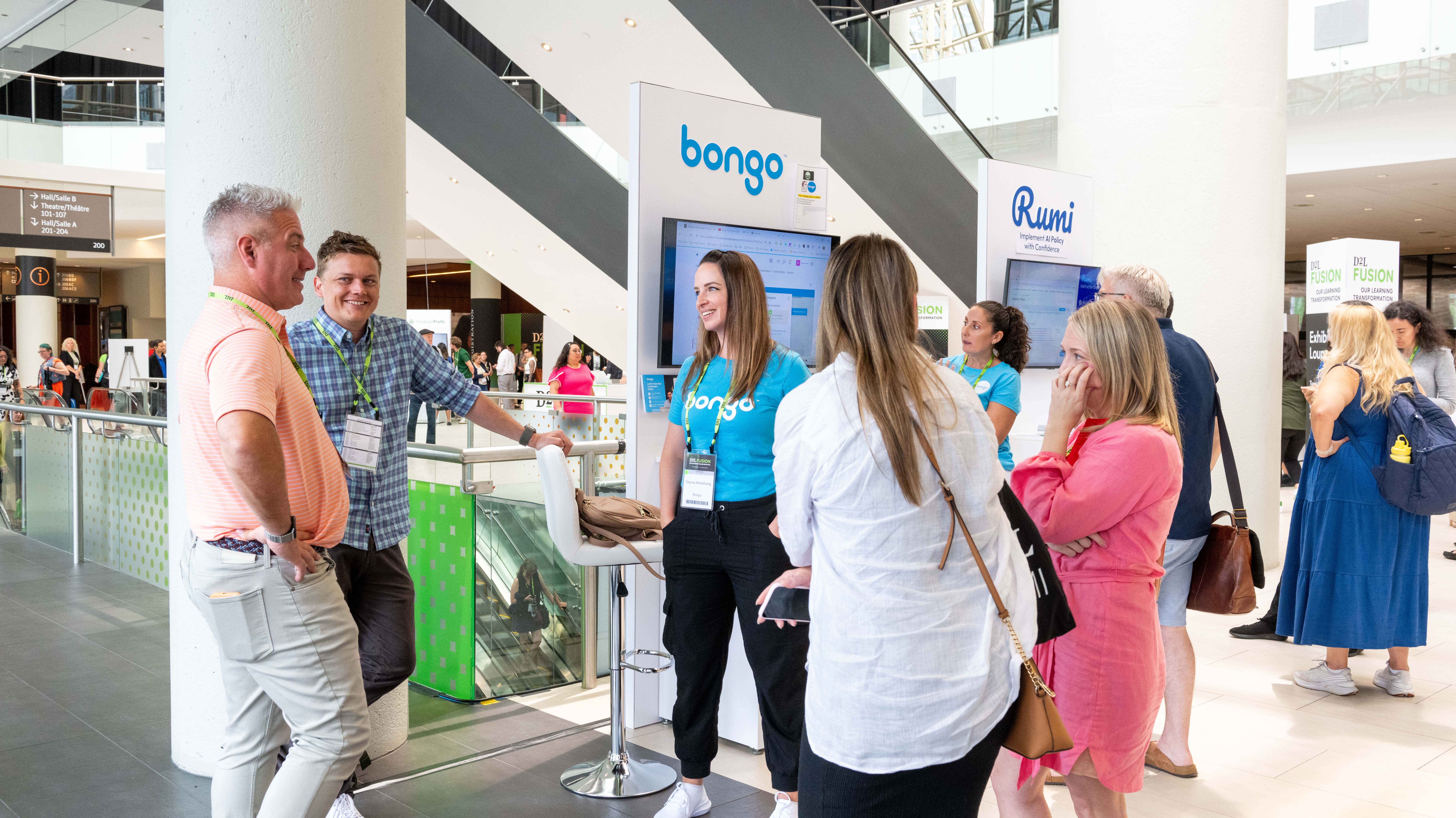 Group of people conversing and engaging near booths labeled 'bongo' and 'Rumi' at a conference or expo.