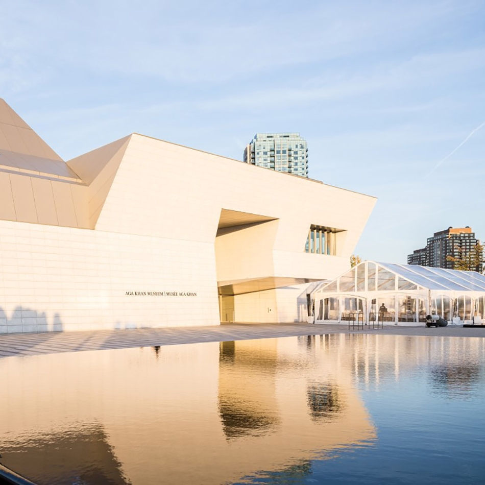 Modern white geometric building with a large reflecting pool in front under a clear blue sky.