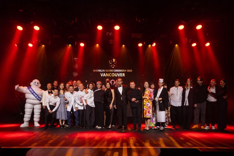 Group of chefs, event staff, and the Michelin Man mascot posing on stage under red and yellow lights at the Michelin Guide Ceremony 2023 in Vancouver.