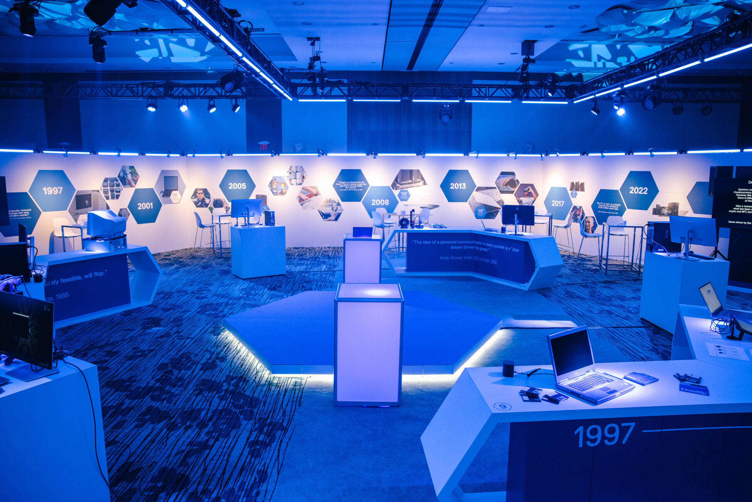 Blue-lit exhibition space showing a timeline wall from 1997 to 2022 with technology displays including laptops and monitors.