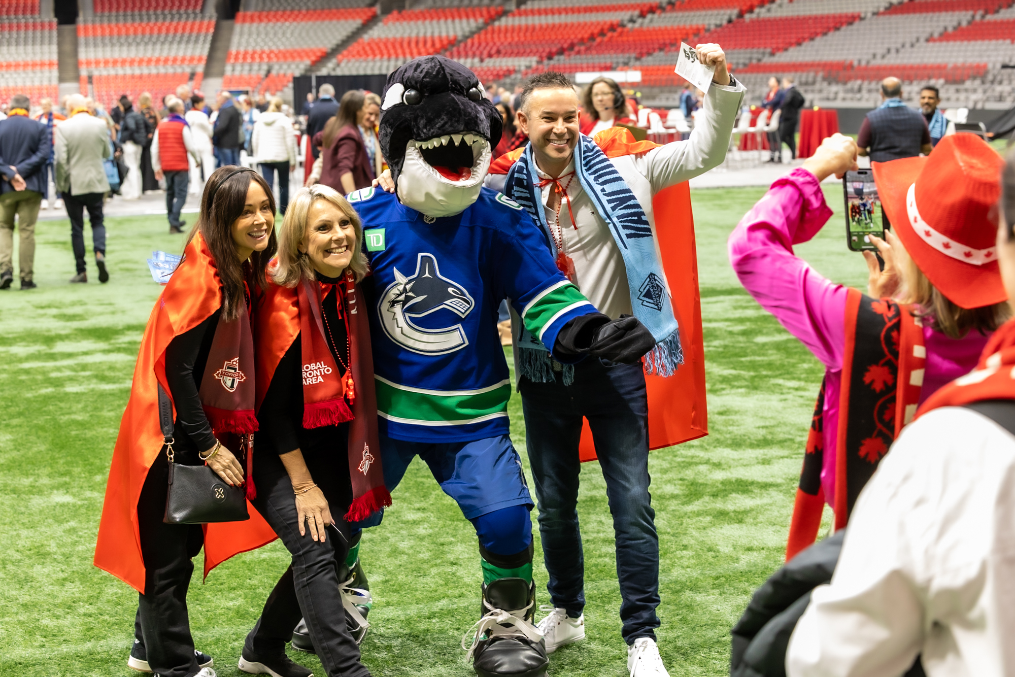 Three people posing with a Vancouver Canucks mascot on a sports field as another person takes their photo.