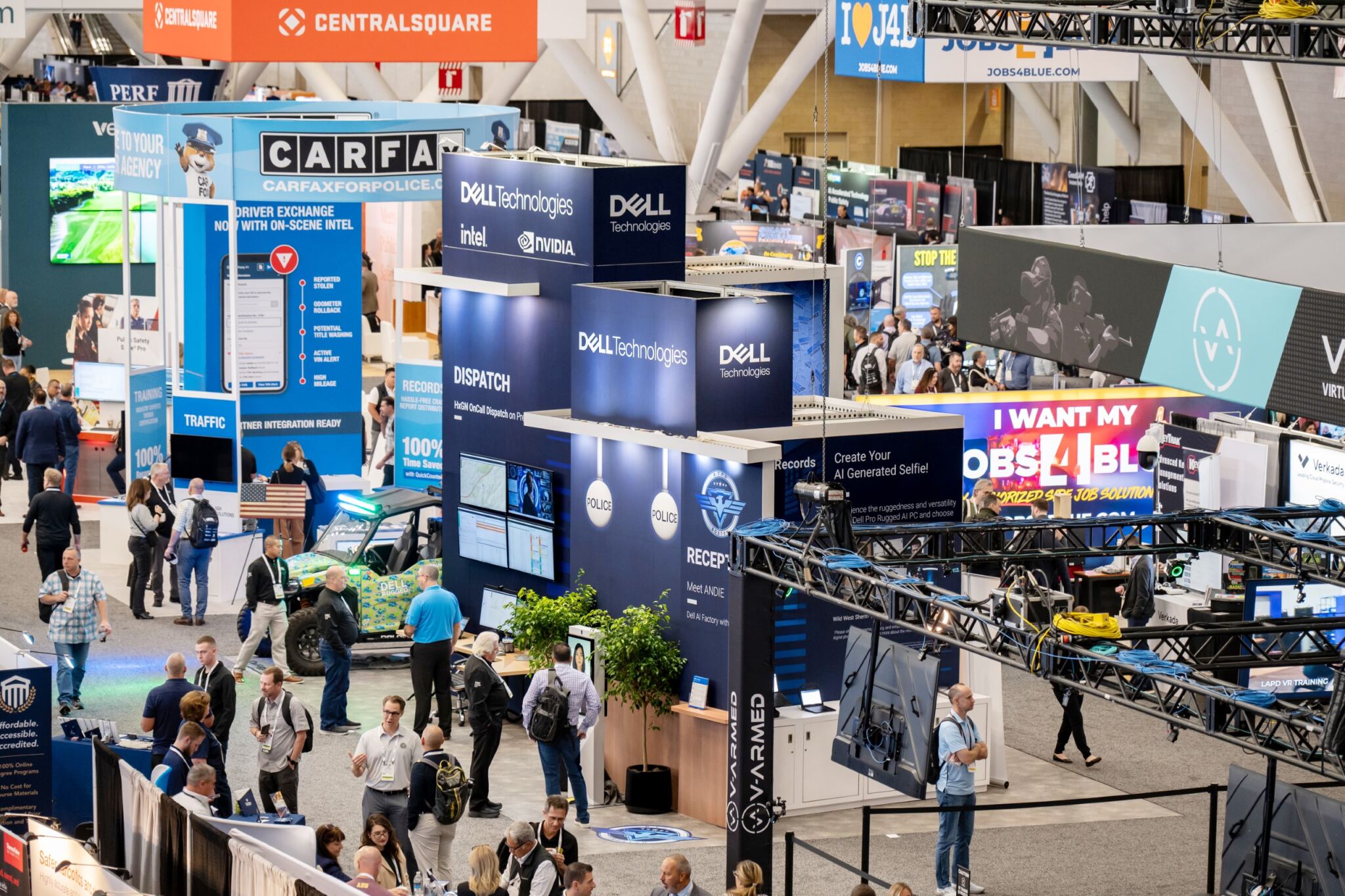 Busy exhibition hall with multiple booths including Dell Technologies and CARFAX, featuring tech displays and attendees.