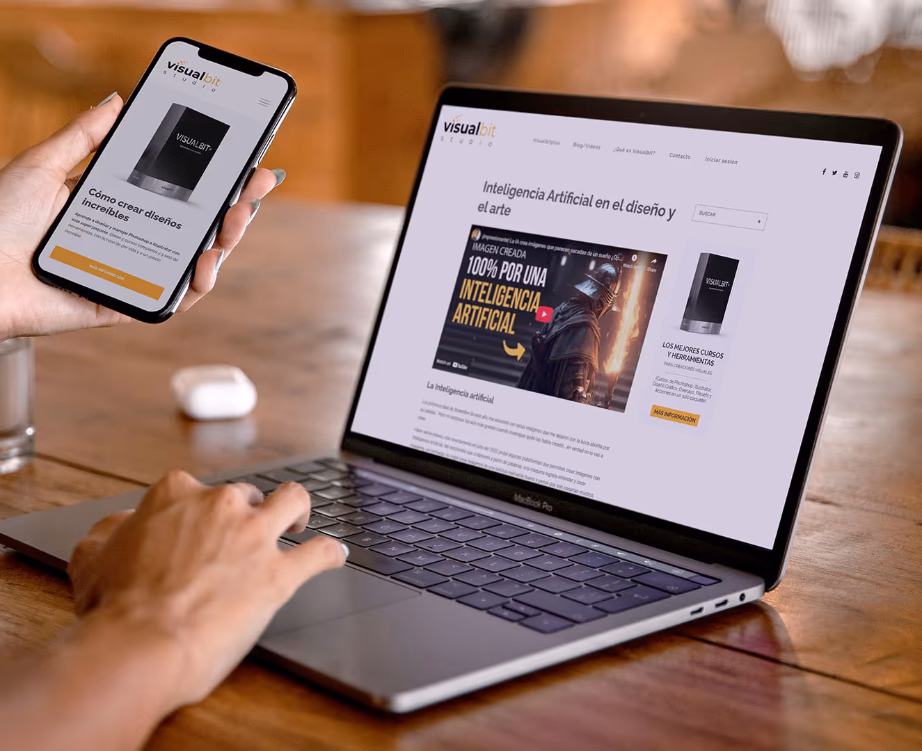 Person using a MacBook Pro and holding a smartphone displaying the Visualbit Studio website with content about artificial intelligence and design.