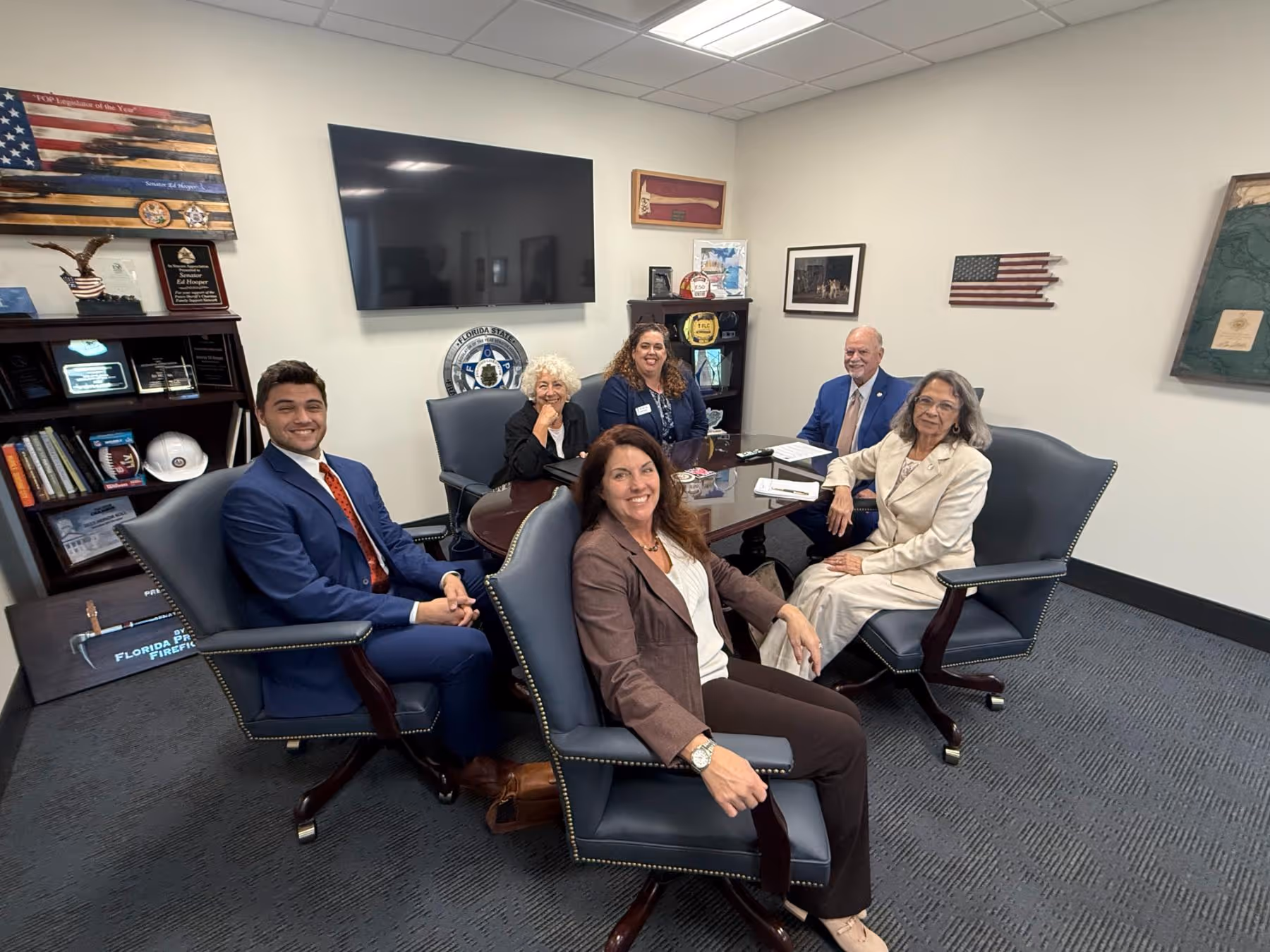 Six people of diverse backgrounds seated around a conference table in a professional office, smiling at the camera.
