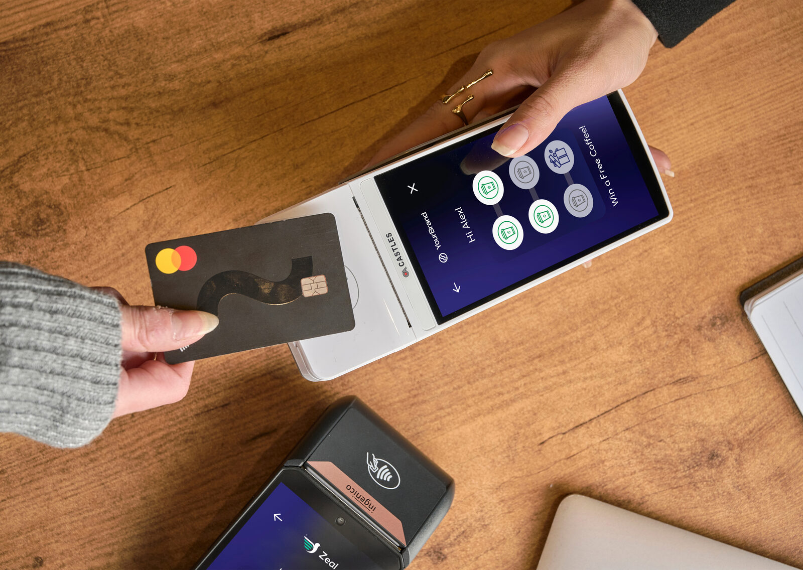 A customer taps a Mastercard on a Zeal-enabled Castles payment terminal showing a personalised loyalty stamp card