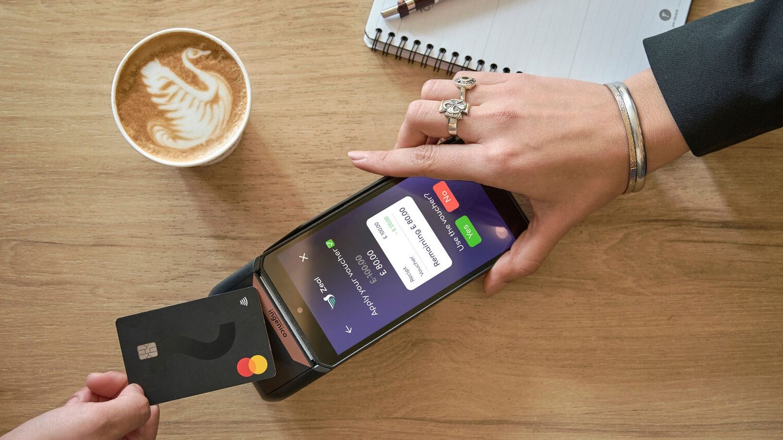 Contactless card payment on a terminal beside a coffee and notebook