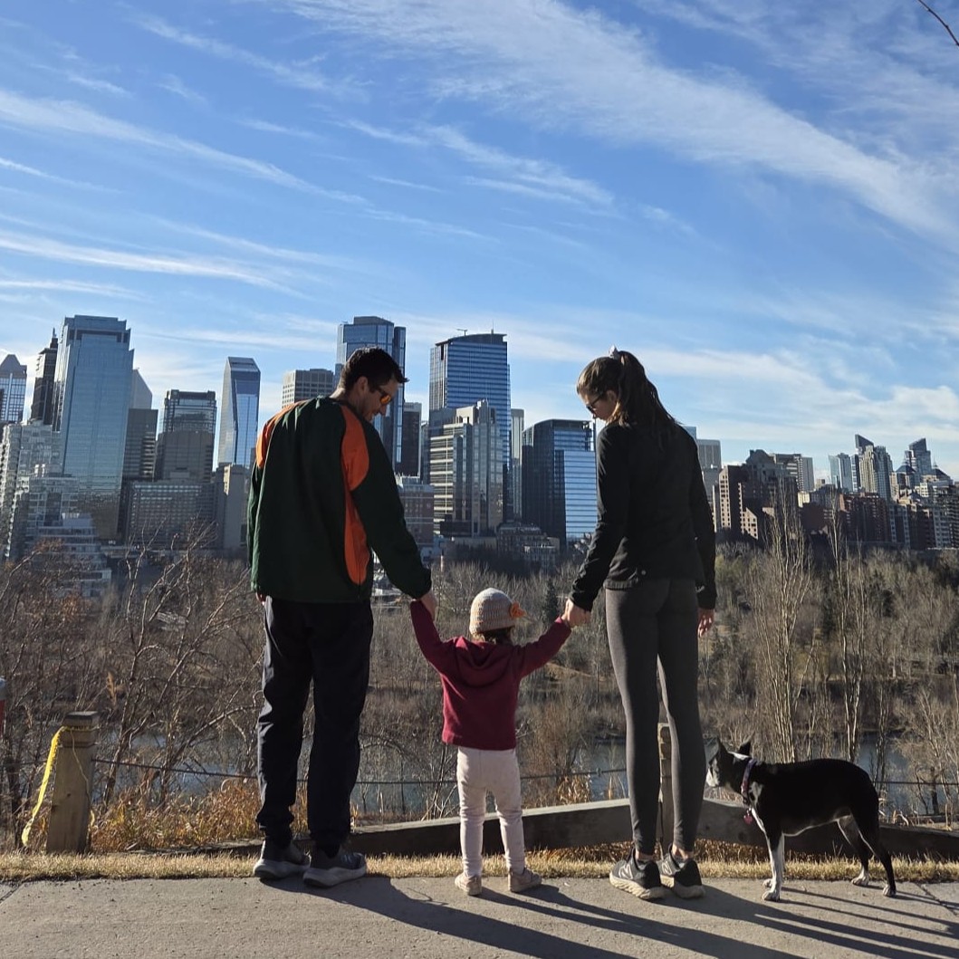 A mom and dad walking with their daughter along a treed path