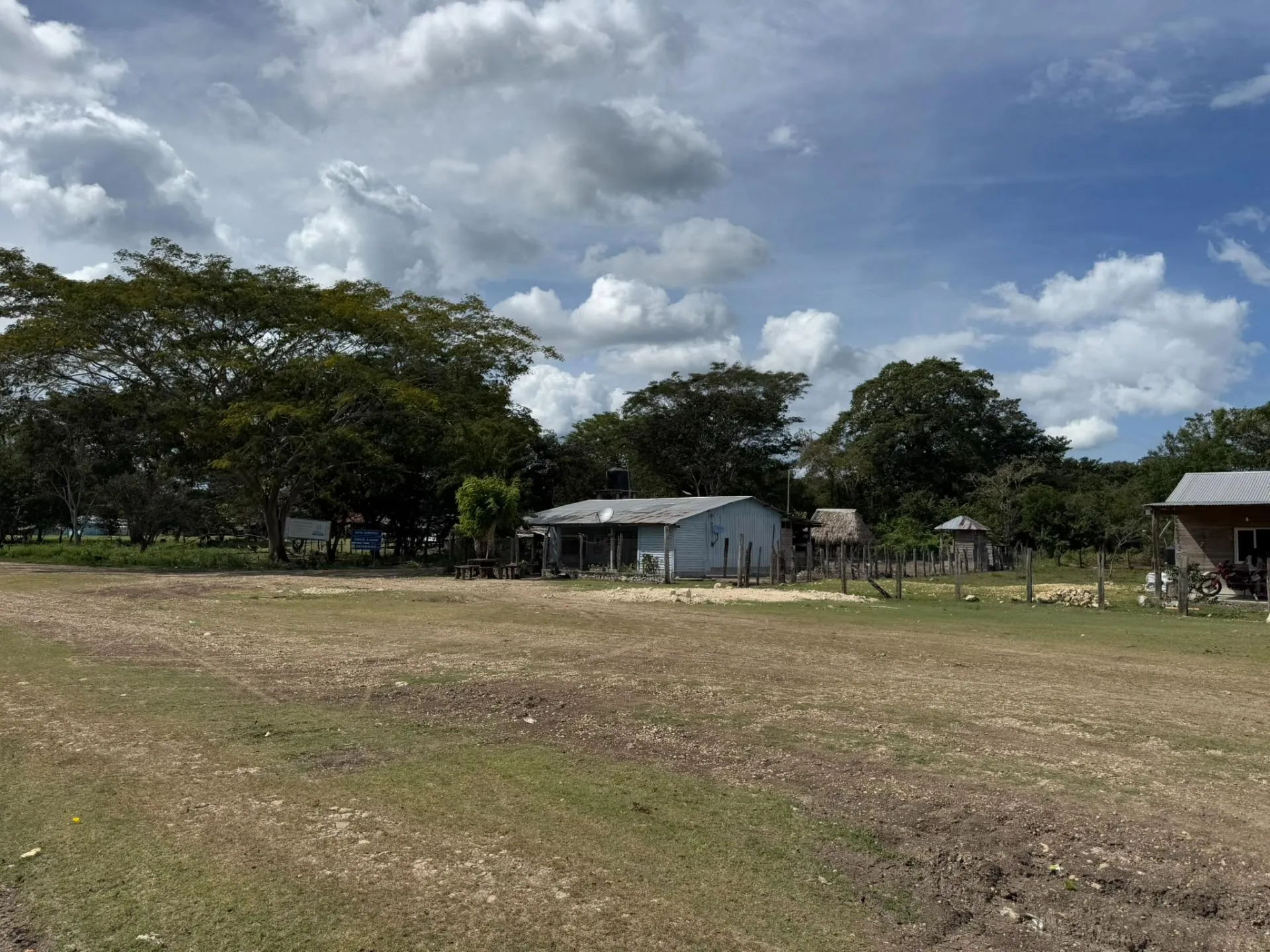 Rural village scene with scattered wooden houses, trees, and a partly cloudy blue sky.