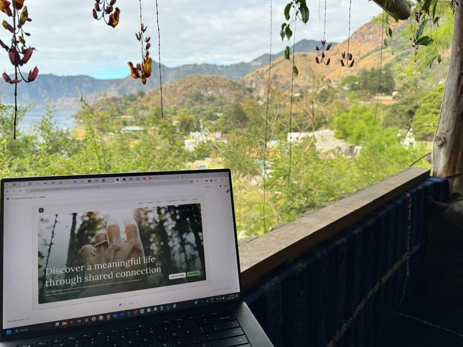 Laptop on a balcony showing a webpage with text about meaningful life, overlooking green hills and mountains.