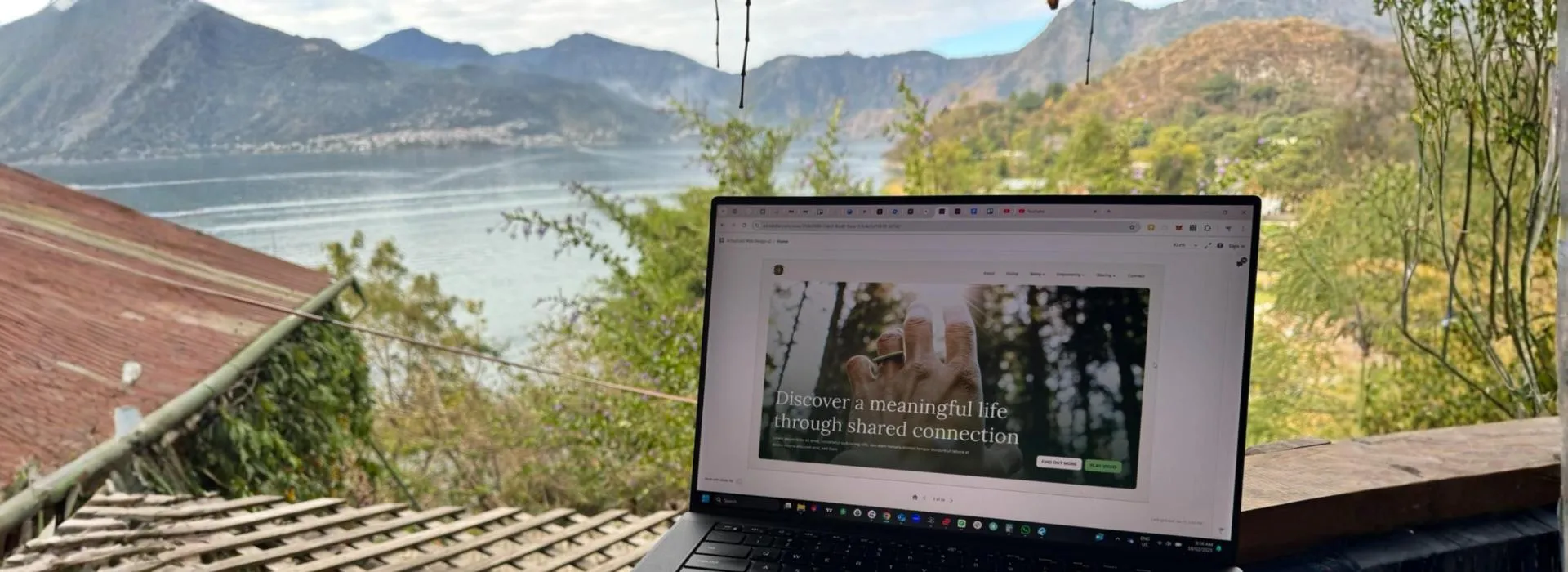 Laptop displaying a website with the text 'Discover a meaningful life through shared connection' set against a scenic lake and mountains background.