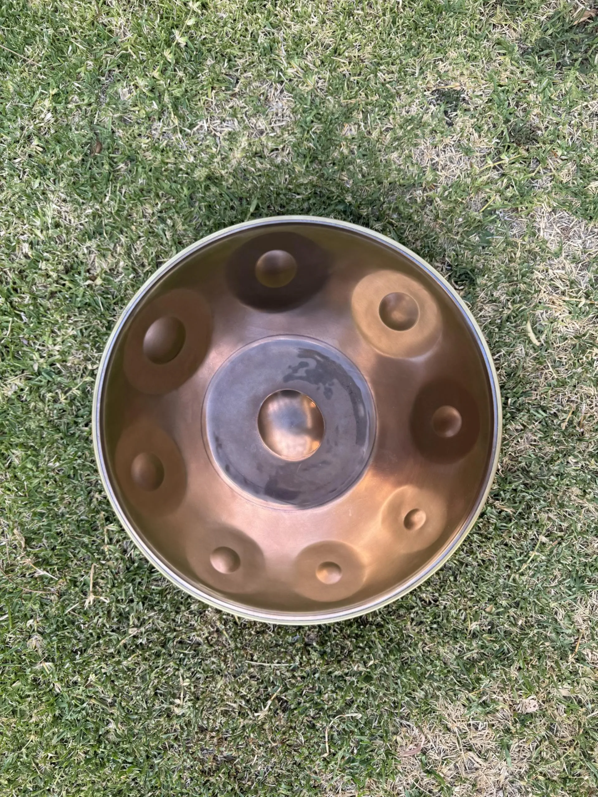Handpan musical instrument placed on green grass, viewed from above.