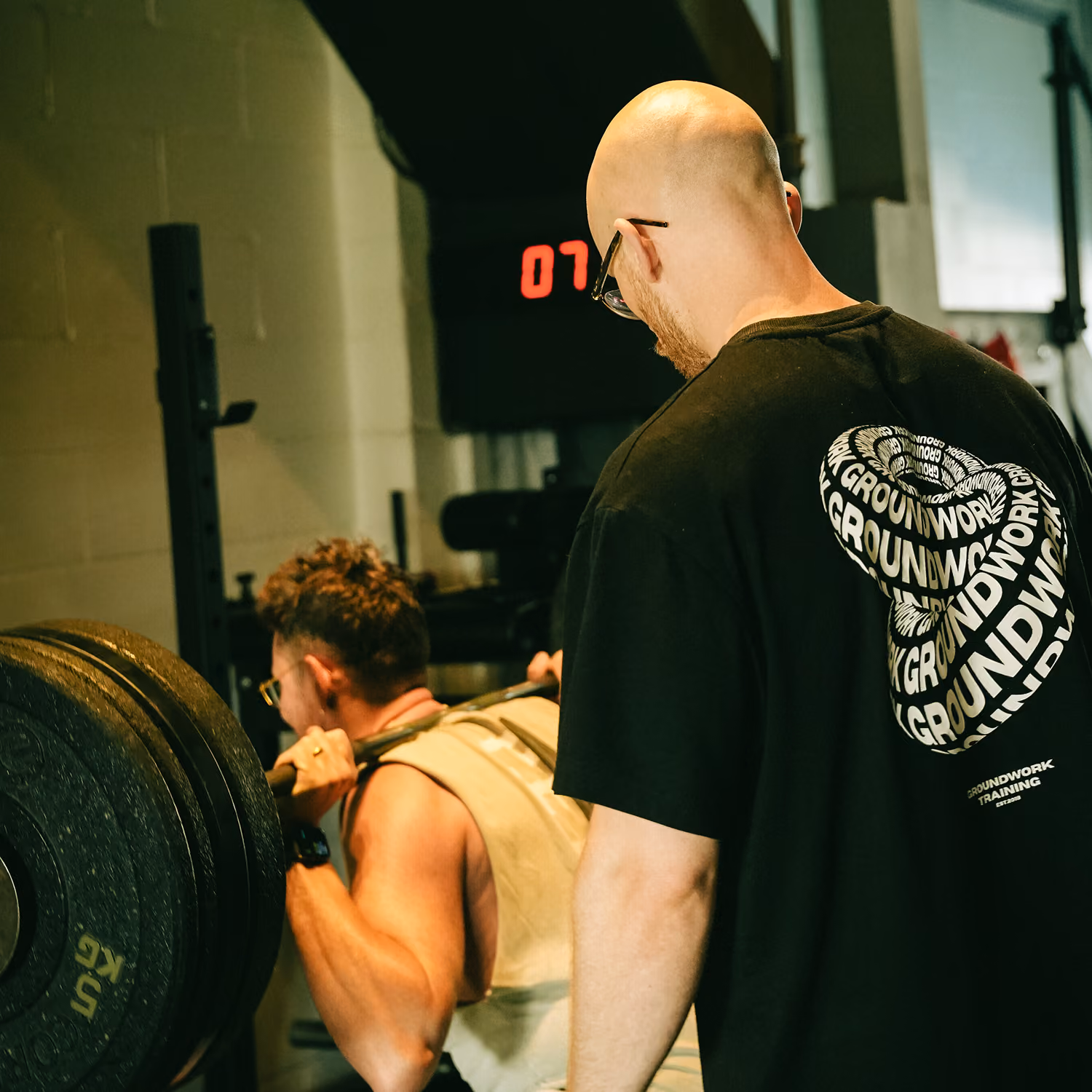 Trainer watches man lifting a heavily weighted barbell during a gym workout session.