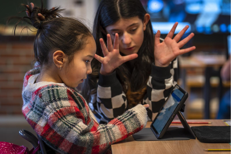 To elever som diskuterer en hoderegningsoppgave. Hun ene holder frem 10 fingre mens hun andre leser oppgaven høyt fra en skjerm.