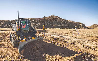 Large bulldozer pushing a mound of dirt on a construction site with mountainous terrain in the background.