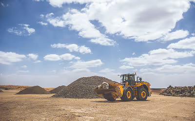 Yellow front loader moving a pile of gravel on a construction site under a partly cloudy sky.