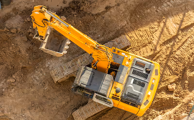 Top view of a yellow excavator with a bucket on a dirt construction site.