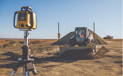 Construction site with a bulldozer moving dirt and a surveying instrument on a tripod in the foreground.