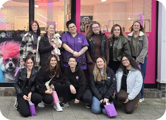 Group of eleven women posing outside a pet store, one holding a small white dog.