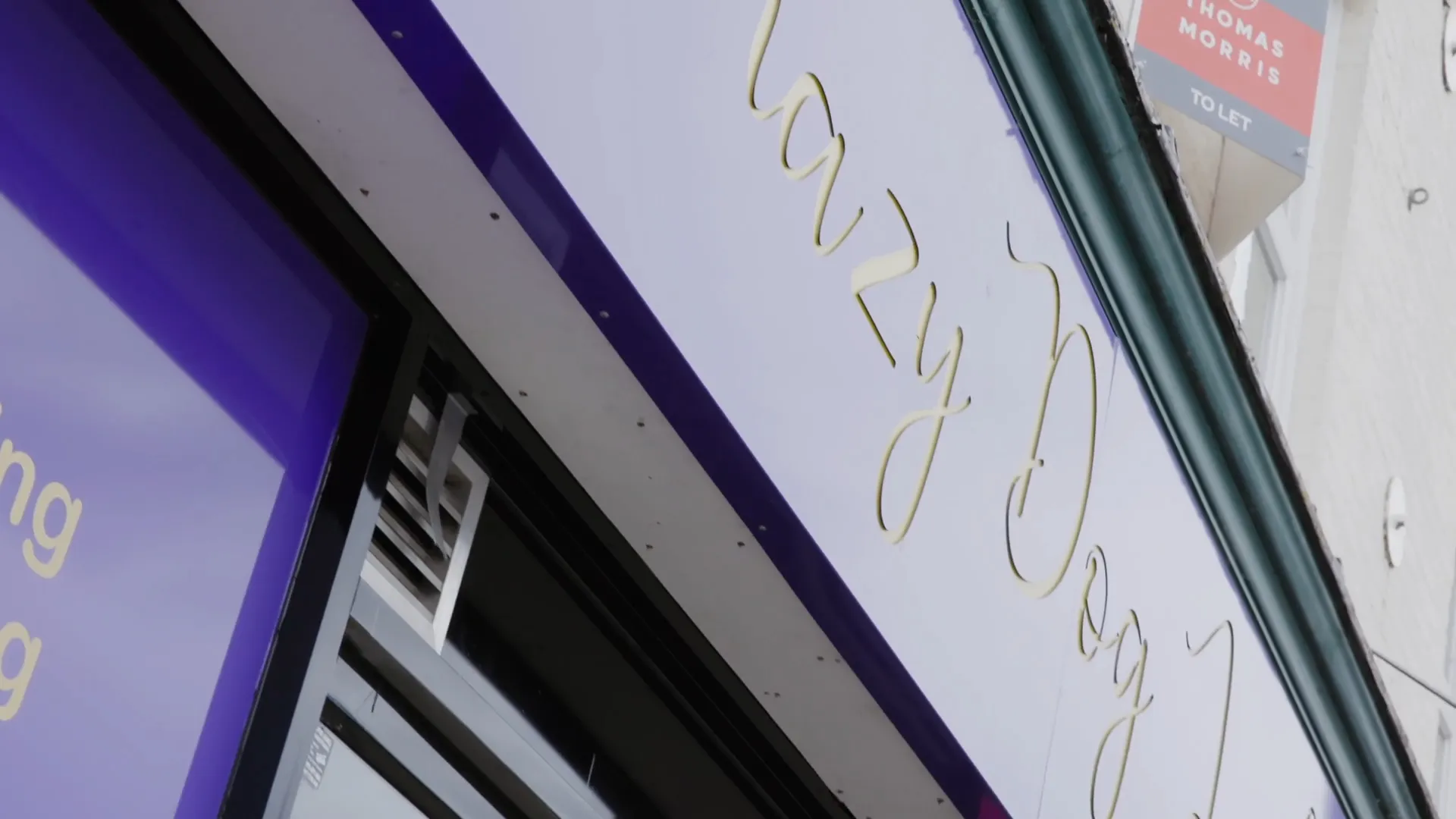 Close-up of a business sign with partially visible gold cursive text on a white and purple background.