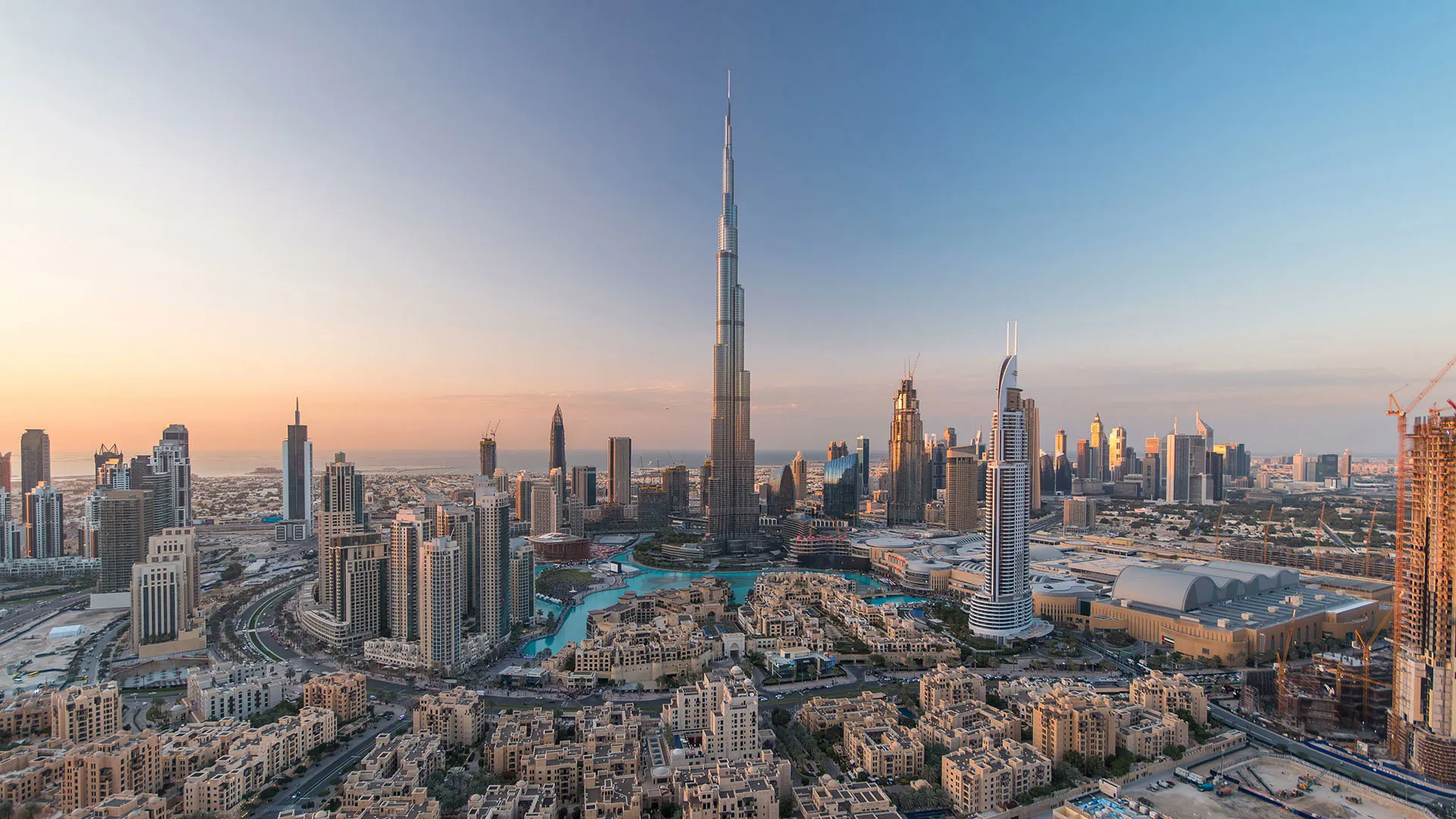 Panoramic view of Dubai skyline at sunset with Burj Khalifa towering over surrounding skyscrapers and urban buildings.