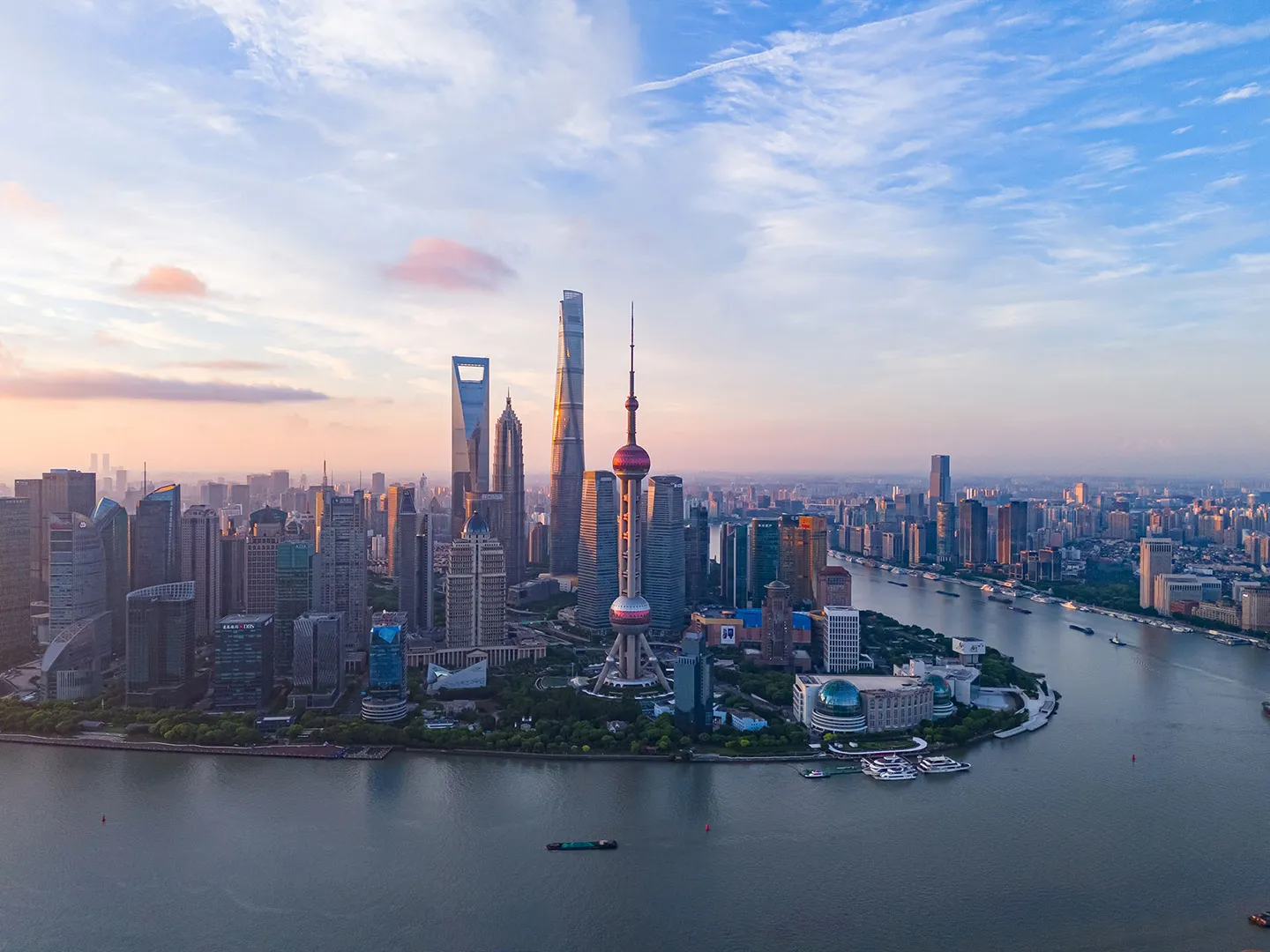 Shanghai skyline at sunset featuring the Oriental Pearl Tower, Shanghai Tower, and Huangpu River.