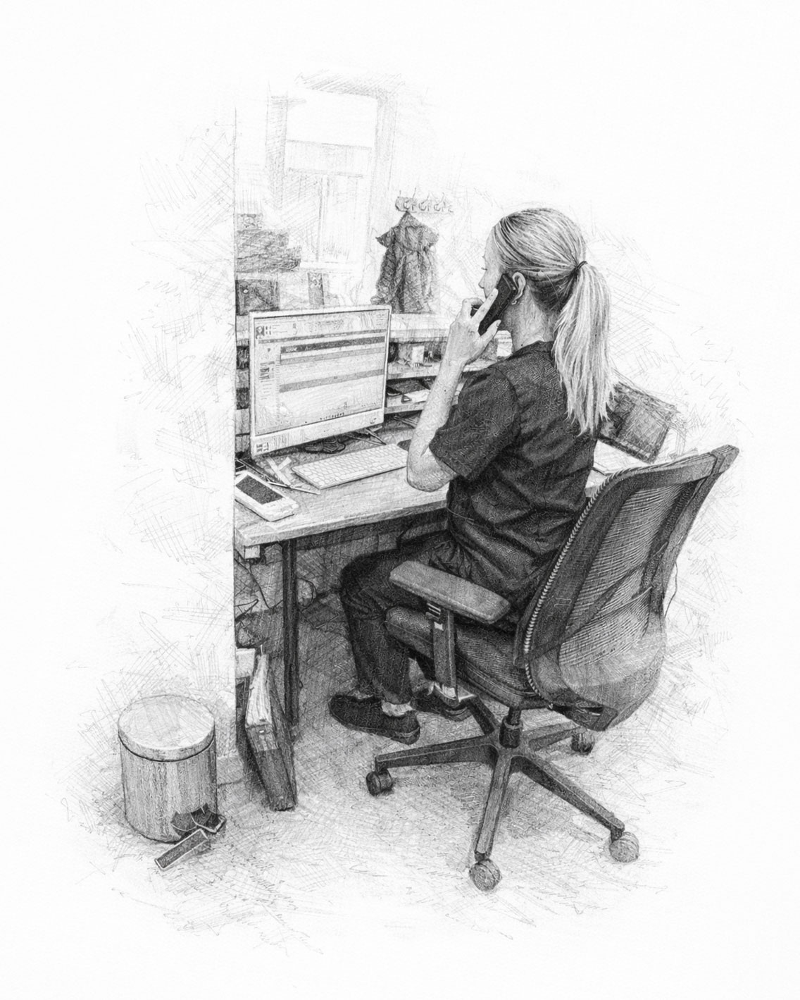A person sits at a desk, talking on a phone while looking at a computer screen.