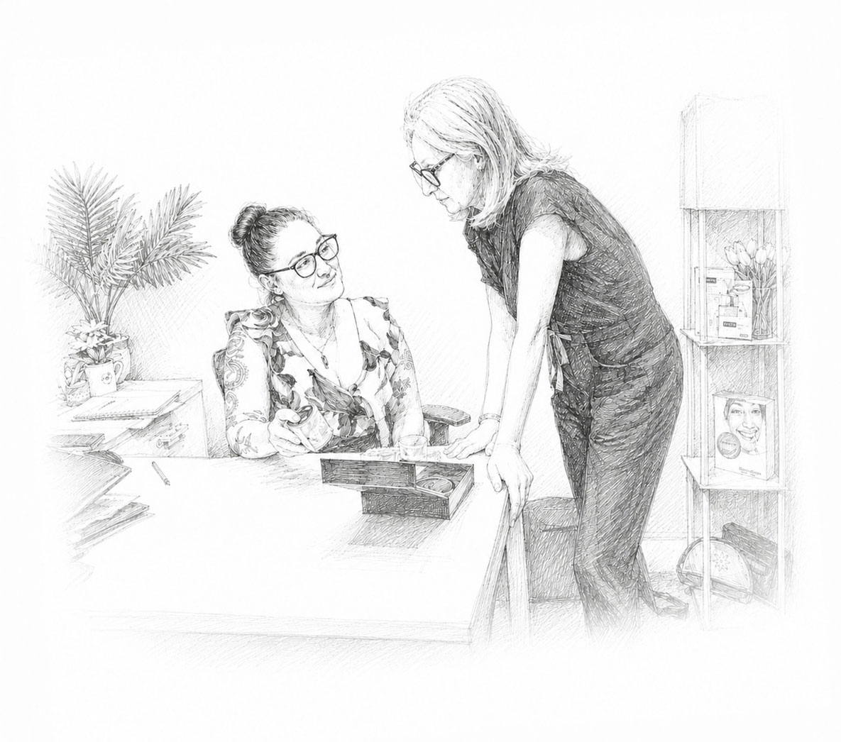 Two women in an office, one sitting and writing, the other standing and talking.