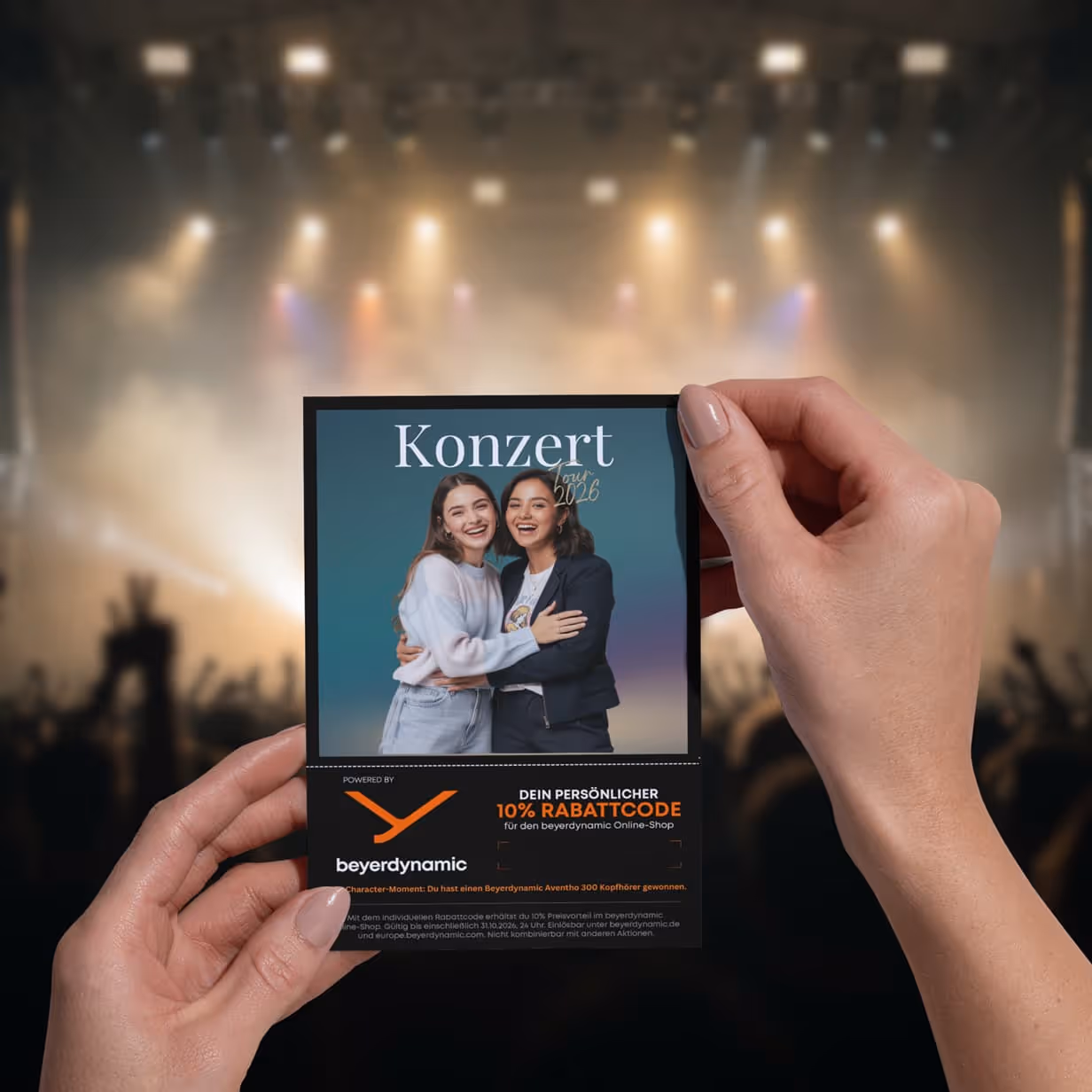 Two hands hold a photo print featuring a contest message and a discount code in front of a concert stage.