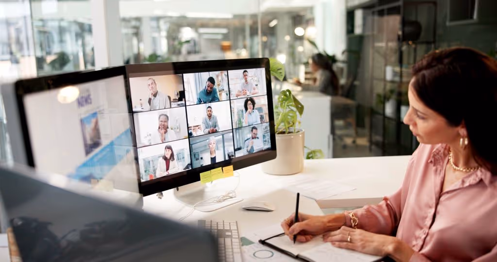 Woman participating in virtual video conference with multiple colleagues on screen