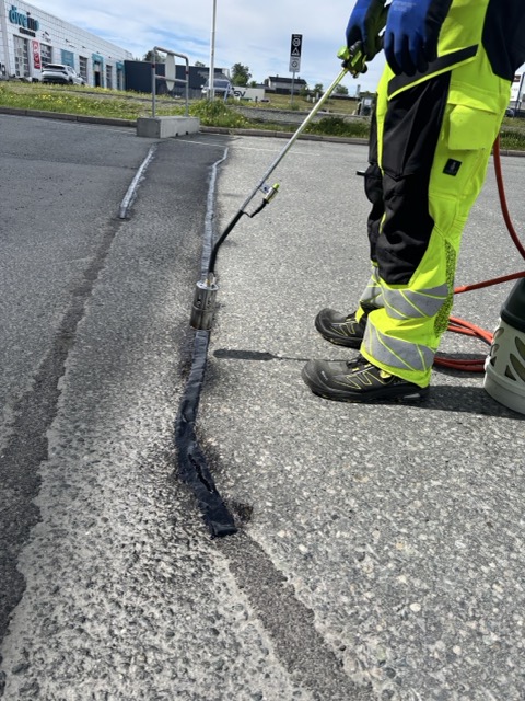 En arbeider varmer asfaltfylling med gass for reparasjon av sprekker i asfalten på veien.
