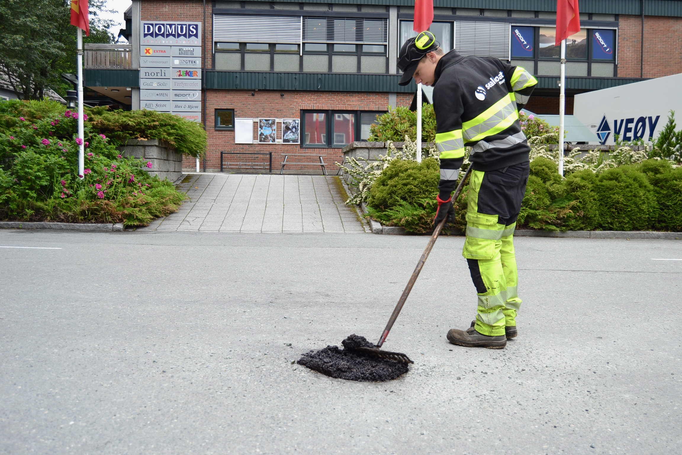 Arbeider i refleksklær reparerer asfalt med en spade på en gate i bymiljø.