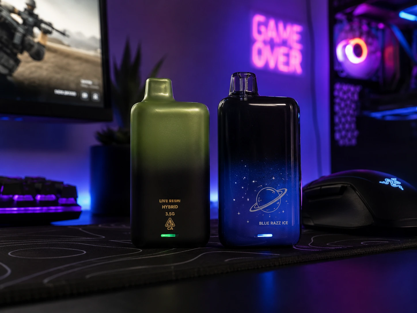 Live resin hybrid THC disposable vape and Blue Razz Ice nicotine vape resting on a dark gaming desk pad next to a PC monitor, keyboard, and gaming mouse.