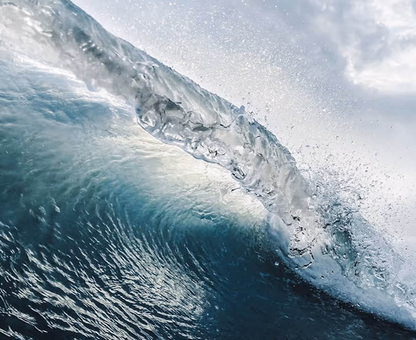 Close-up of a translucent ocean wave curling with splashing water droplets.