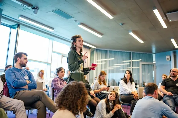 Engaged woman leading a discussion during a student workshop with a diverse group seated in a modern conference room, emphasizing collaboration and active learning.