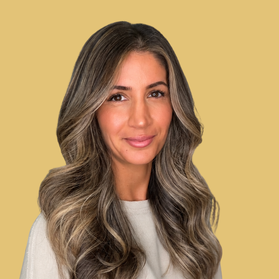 Smiling woman with long wavy hair wearing a light-colored top against a beige background.