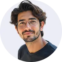 Portrait of a young man with dark wavy hair and a beard, wearing round glasses and a black shirt, smiling slightly against a plain light background.