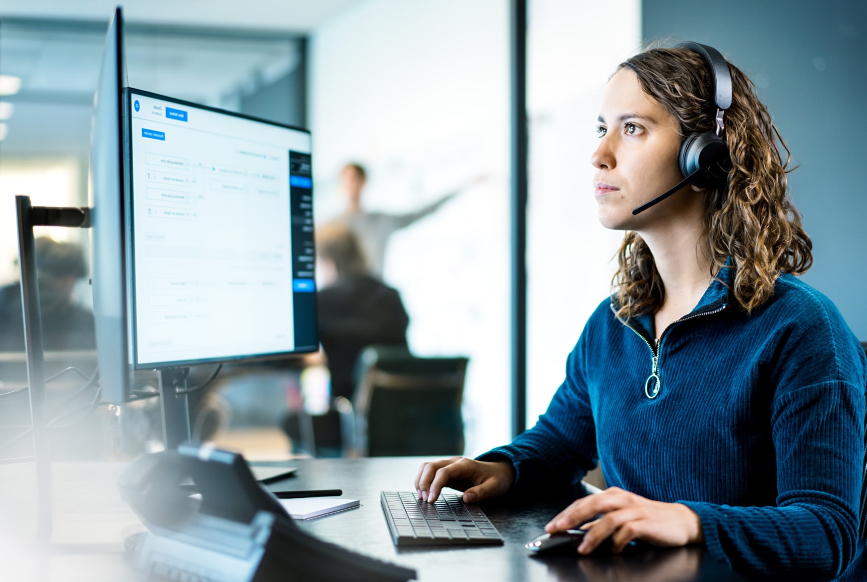 Supportmitarbeiterin mit Headset arbeitet konzentriert am Dual-Monitor-Setup